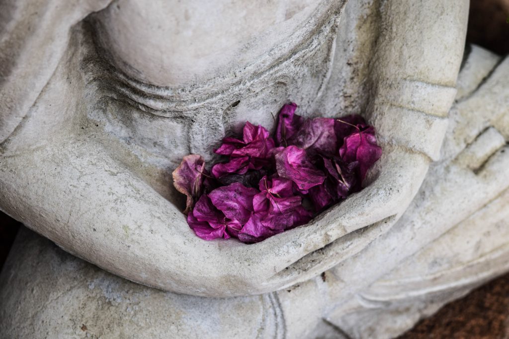 Statue in meditativer Pose mit Blütenblättern